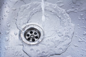 Water draining at sink background. Water flowing drain in washbasin after the drain was clogged